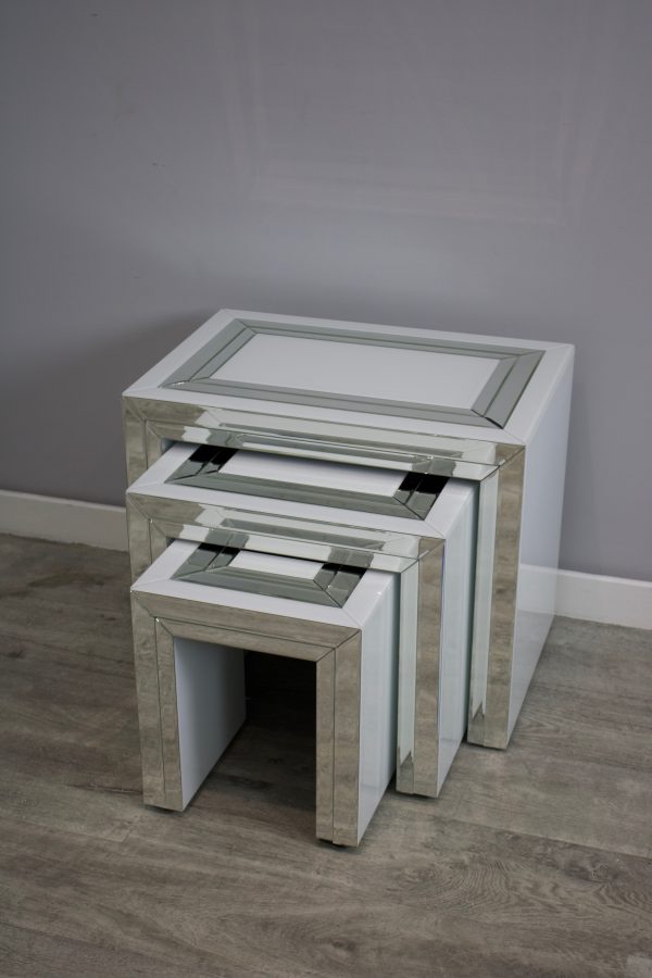 Set of three nesting tables with a mirror-like finish on a gray floor against a gray wall.