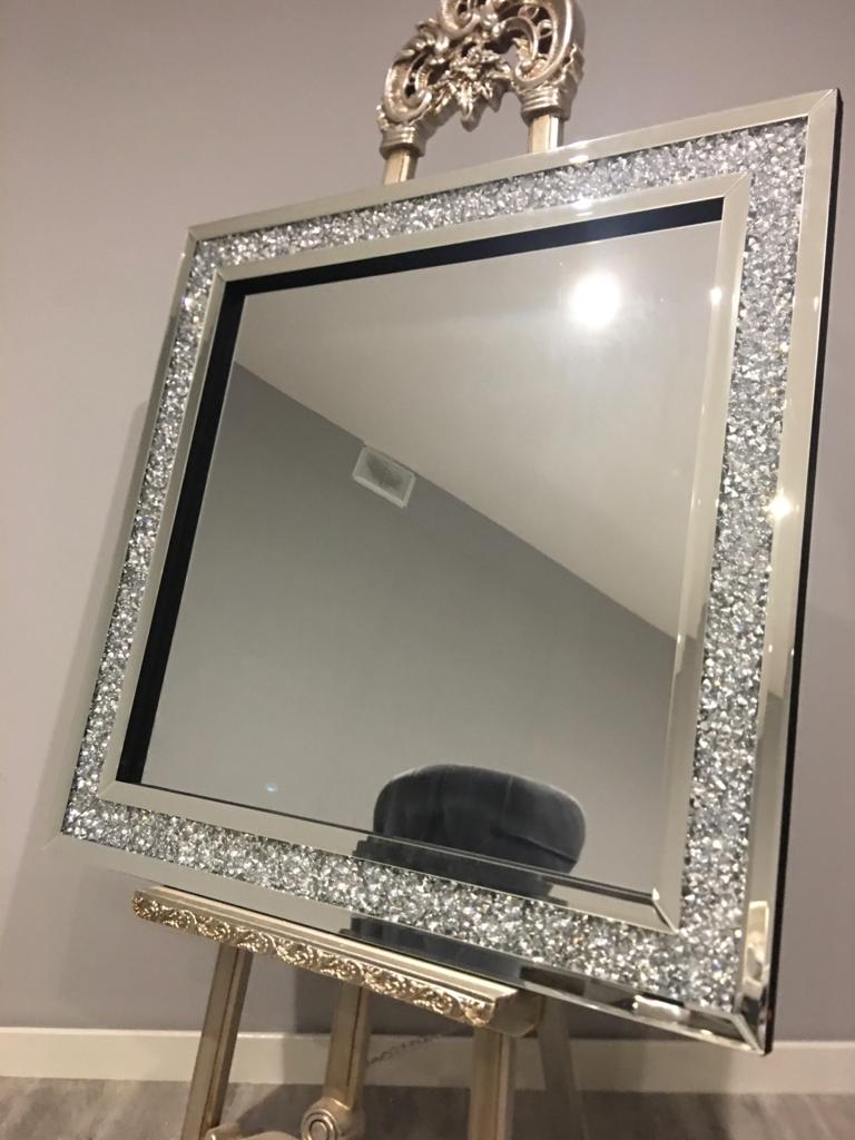 Decorative mirror with a sparkling frame on an easel against a plain wall.