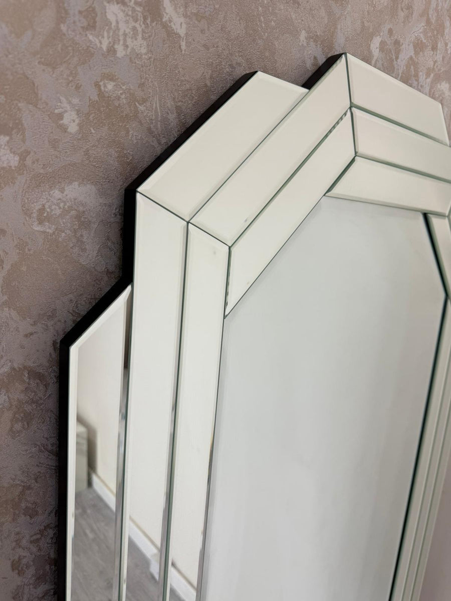 Hexagonal mirror with a black frame on a textured wall.