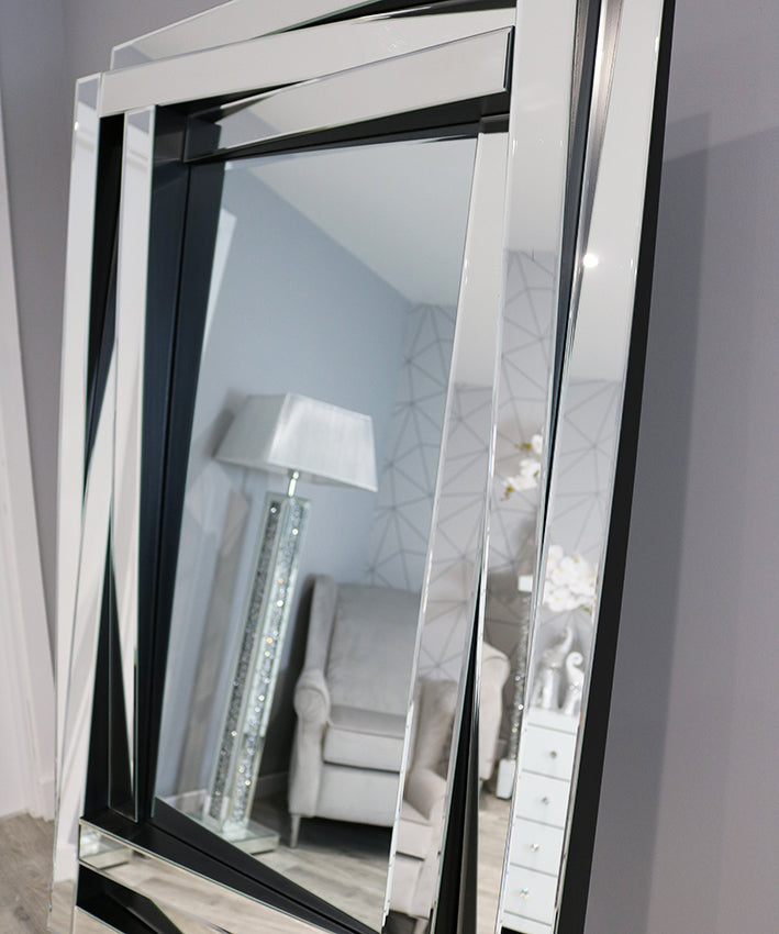 Large floor mirror with black frame reflecting a room with furniture and decor.
