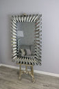 Decorative mirror with unique design on a stand against a gray wall.