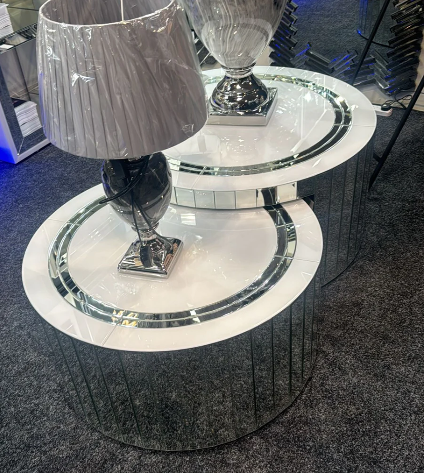 Round mirrored coffee table with silver base and lamp on a dark floor.