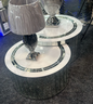 Round mirrored coffee table with silver base and lamp on a dark floor.