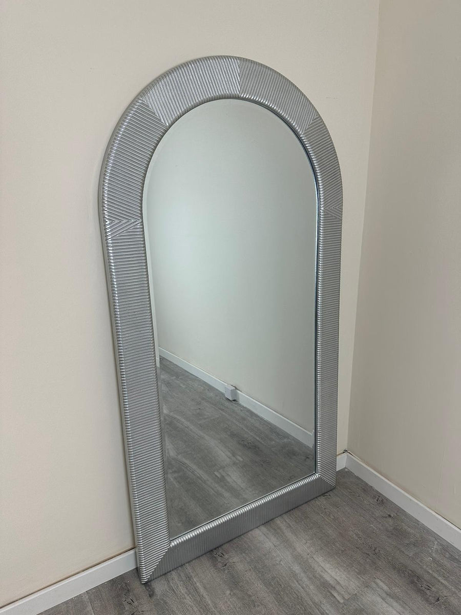 Silver-framed mirror leaning against a white wall.