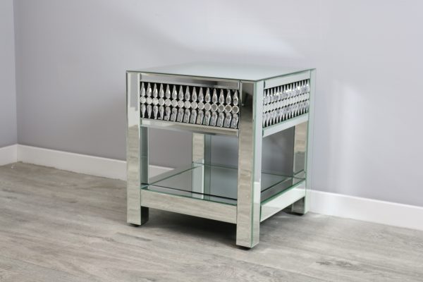 Mirrored side table with glass shelf on a wooden floor against a gray wall.