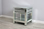 Mirrored side table with glass shelf on a wooden floor against a gray wall.