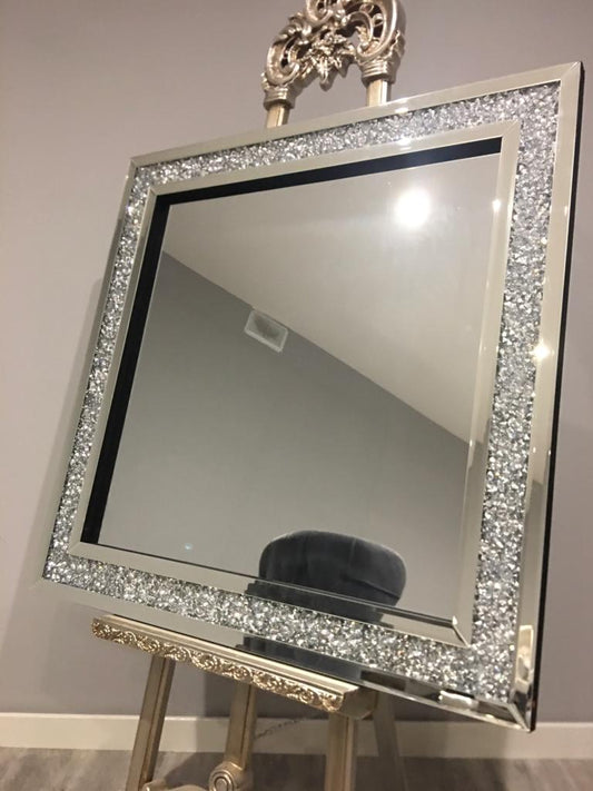 Decorative mirror with a sparkling frame on an easel against a plain wall.