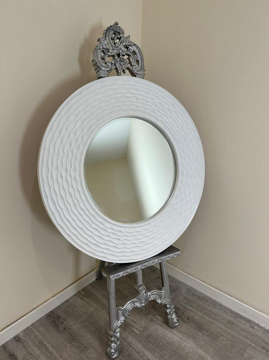 Decorative round mirror with intricate design on a stand against a beige wall.
