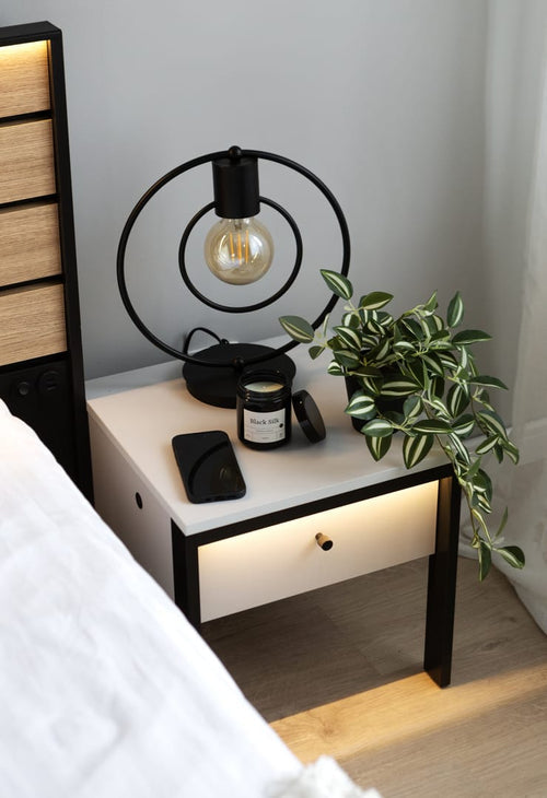 Nightstand with lamp, phone, and plant next to a bed