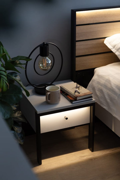 Nightstand with a lit drawer next to a bed in a bedroom setting