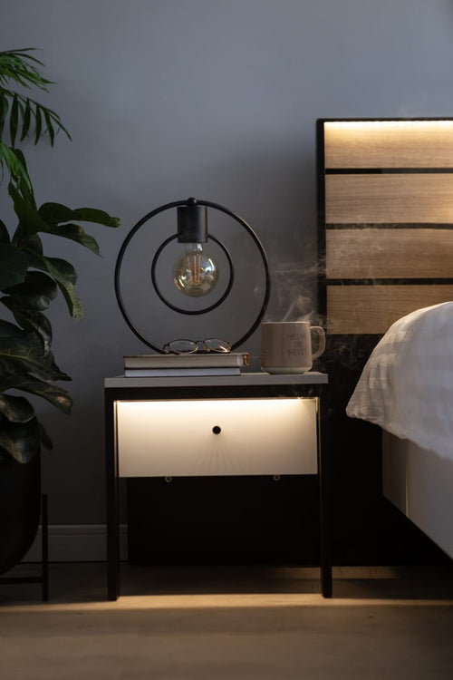 Nighstand with decorative lamp and plant next to a bed