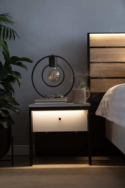 Nighstand with decorative lamp and plant next to a bed
