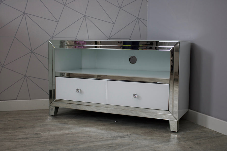 Silver mirrored TV stand with white drawers against a geometric-patterned wall.