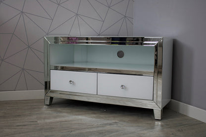 Silver mirrored TV stand with white drawers against a geometric-patterned wall.