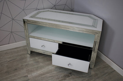 Small corner TV stand with mirrored top and drawers against a geometric-patterned wall.