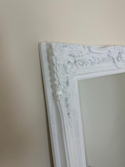 Decorative white mirror with intricate frame against a plain wall