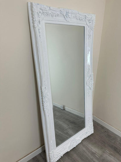 White ornate mirror leaning against a beige wall.