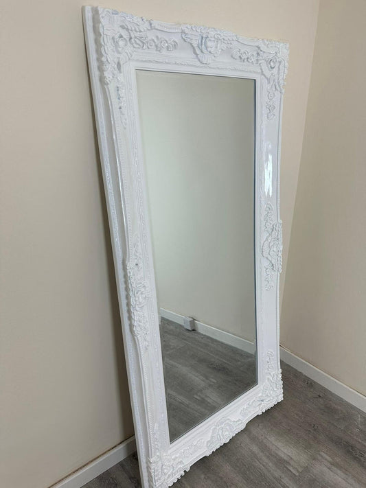 White ornate mirror leaning against a beige wall.