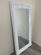 White ornate mirror leaning against a beige wall.