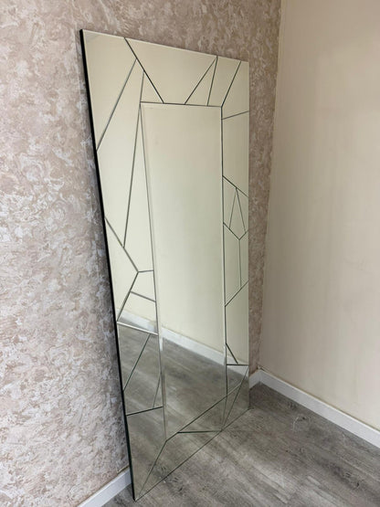 Tall mirror with geometric frame leaning against a textured wall.