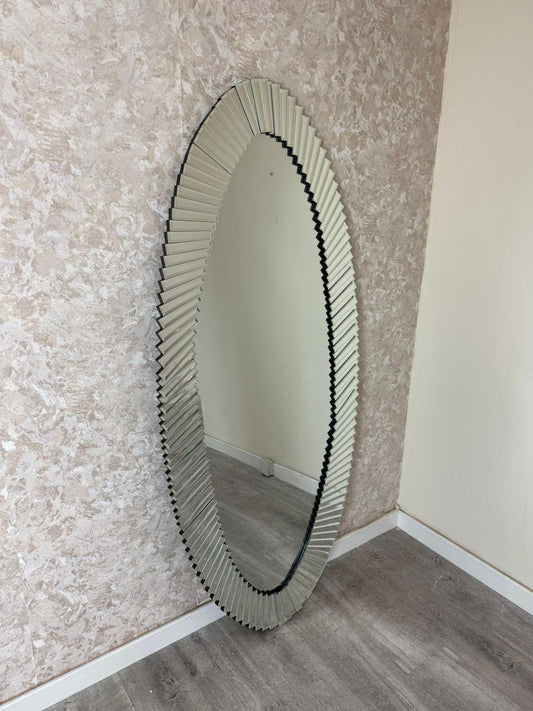 Oval mirror with decorative frame leaning against a textured wall.