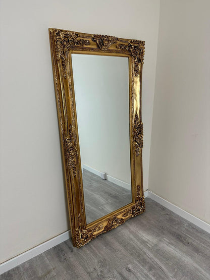 Decorative gold-framed mirror leaning against a white wall.