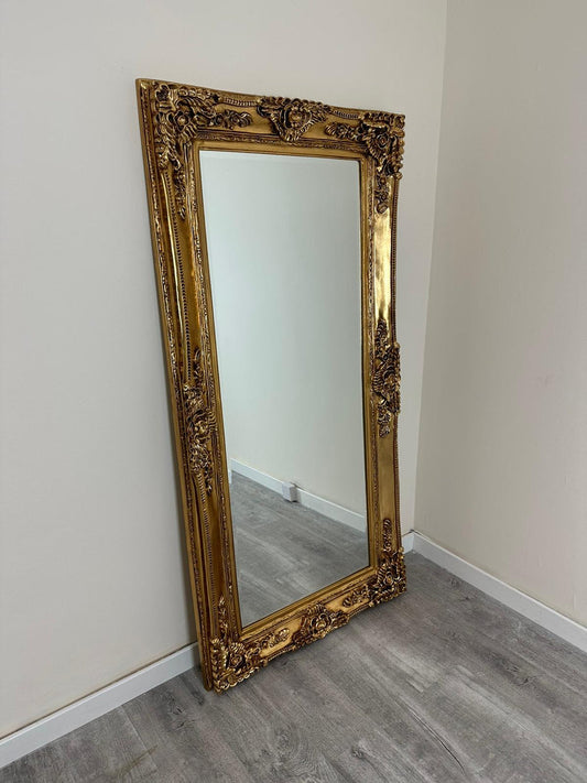 Decorative gold-framed mirror leaning against a white wall.