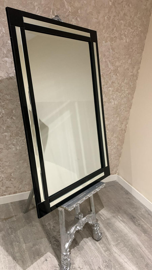 Large mirror with a black frame on a decorative stand against a textured wall.