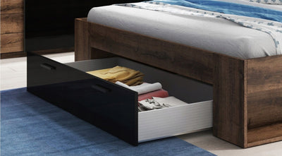 Wooden bed with open drawer revealing bedding and pillows on a blue carpet.