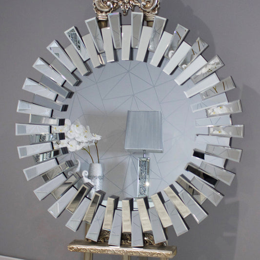 Decorative round mirror with a unique frame design on a gray wall.