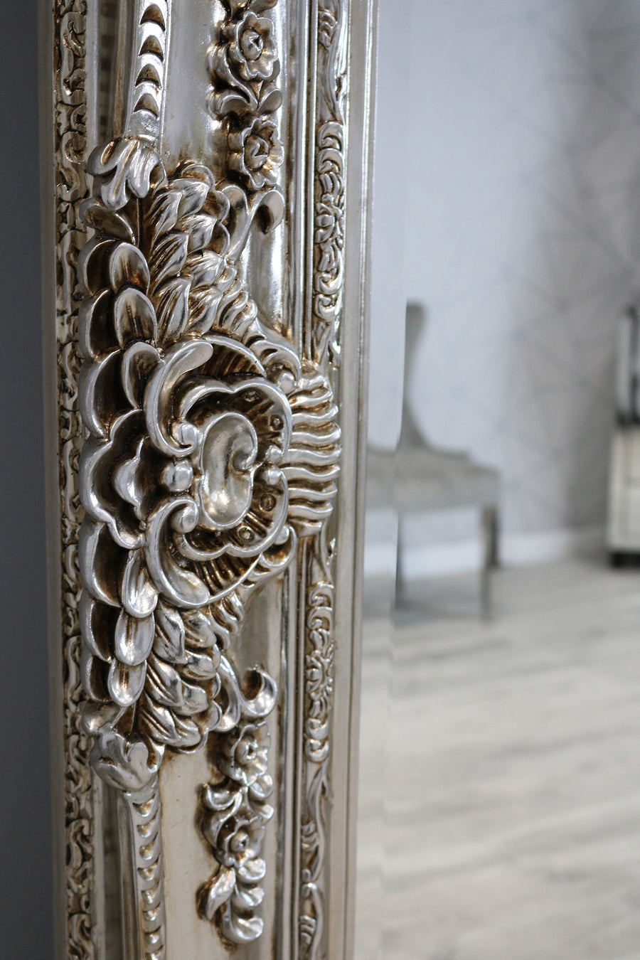 Decorative muted brownish-grey mirror with intricate floral patterns in a room setting.